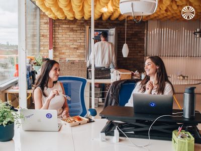 Two white women having lunch at their desks in an office.