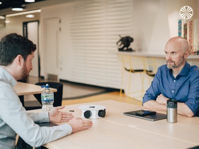 2 people in discussion at a meeting table with devices and water bottles.