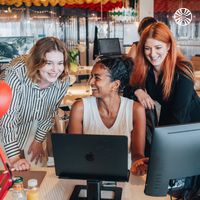 2 white women and one Black woman collaborating at a desk with a laptop in an office.