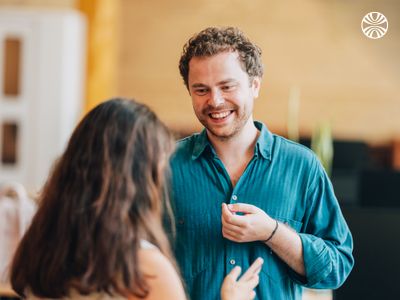 White man and woman talking while gesturing in a hallway, appearing engaged in discussion.