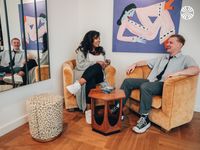 A Black woman and a white man share a casual conversation in a stylish co-working lounge, decorated with vibrant artwork.