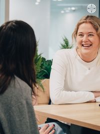 Two colleagues having a one-on-one discussion across a table in a bright meeting room with plants.