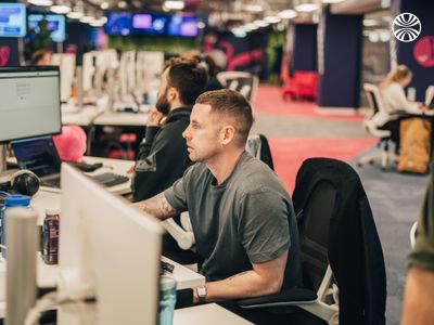 Professional focused on computer work in an open-plan office with carpet and industrial ceiling.