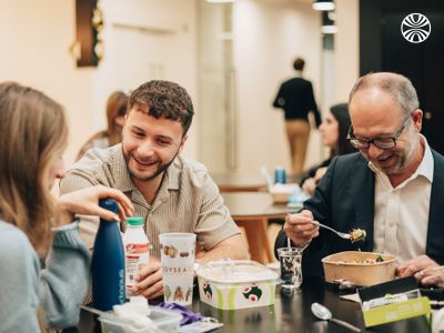 3 colleagues sharing lunch and conversation at a casual office dining area.