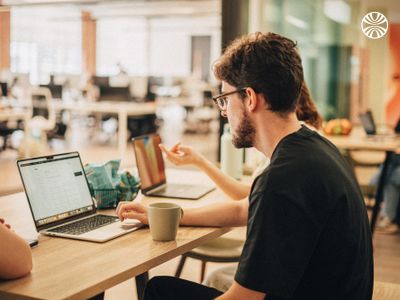 Three coworkers collaborating at a table with laptops and snacks.