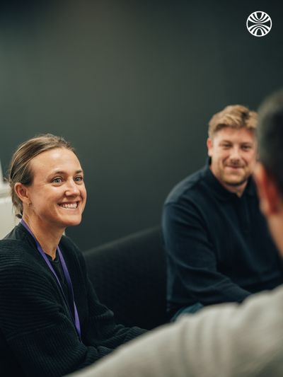 Person smiling during a meeting with colleagues, engaged in conversation.