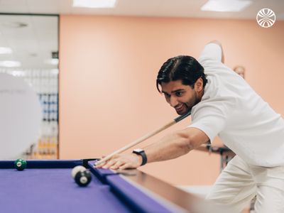 Colleague playing pool in the office break area with a relaxed, focused expression.