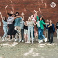 A joyful group of 14 diverse colleagues jumping and striking fun poses on the street outside the office.