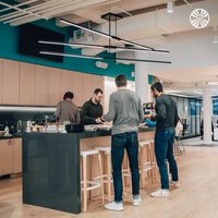 Modern office kitchen area with colleagues gathering at a counter and serving themselves food from a catered buffet..