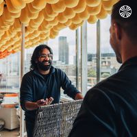 Man with long hair smiling while working or conversing indoors.