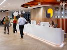 People walking past a large white reception desk. The AlphaSights brand mark hangs from a wall of wooden slats behind the desk. 