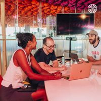 4 people, including a Black woman, collaborating around a laptop at a table.