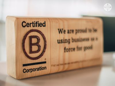 Wooden plaque showing B Corporation certification with text "We are proud to be using business as a force for good."