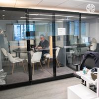 Glass-walled meeting room and workstations in a contemporary office setting with modern furnishings.