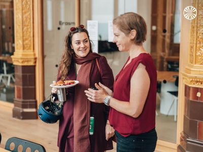 Two white women in conversation near a windowed area in the office.