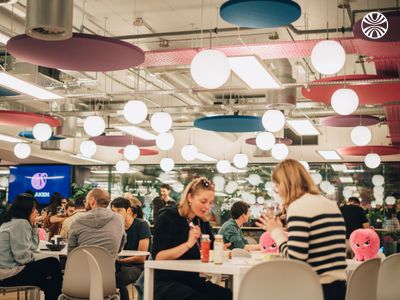 Employees gathered in common area with round tables and industrial ceiling lighting.