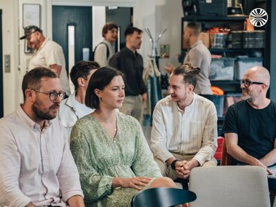 Four white coworkers sitting in a casual meeting room, talking and smiling.