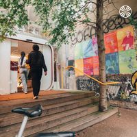 2 Black women entering a graffitied building with various posters on display.