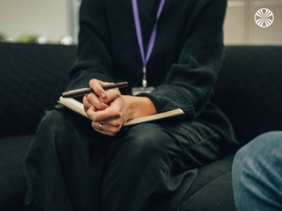 Close-up of hands taking notes in a notebook, with a purple lanyard visible.