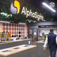 An illuminated AlphaSights logo hangs over a kitchen with breakfast and snack dispensers on an island.