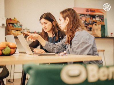 Two women working together on laptops at a table.