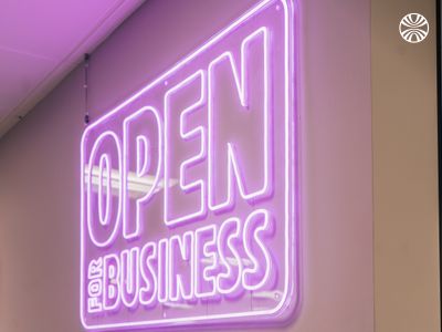 Purple neon sign reading "OPEN for BUSINESS" mounted on an office wall.