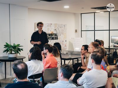 CEO Will Pearce leads the all hands in the Orbital Witness office. The team is seated in front of him.