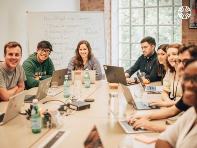 Group of coworkers in a meeting with laptops and a whiteboard.