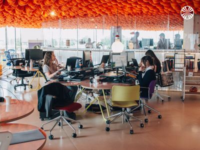 Several people working at desks with computers under an orange ceiling.