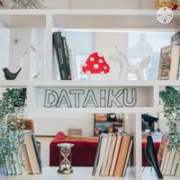 Decorative shelf display featuring books, plants, and whimsical decorations along with "Dataiku" signage.