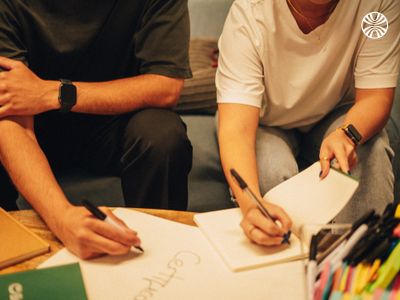 Two people sitting and writing in notebooks.