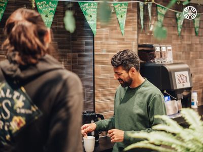 Employee preparing coffee at a break station decorated with St. Patrick's Day banners and plants.