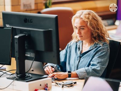 White woman with curly blonde hair focused on her computer in a quiet workspace.