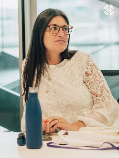 Person with long hair and glasses seated at a desk with their water bottle and lunch.