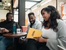 3 Black colleagues laughing and chatting in the co-working space's shared cafe.