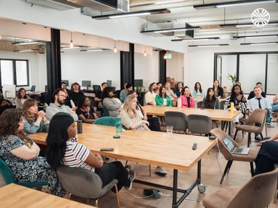 A diverse team listens attentively in a company all-hands meeting in a spacious modern office.