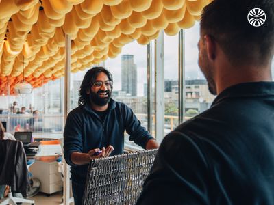 Man with long hair smiling while working or conversing indoors.