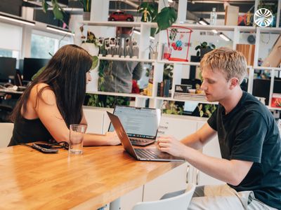 White woman and white man collaborating with laptops in a lively office.