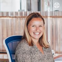 White woman smiling while sitting at a desk with a notebook.