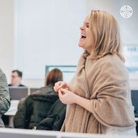 Two team members sharing a lighthearted conversation at their desk in a bright office space.