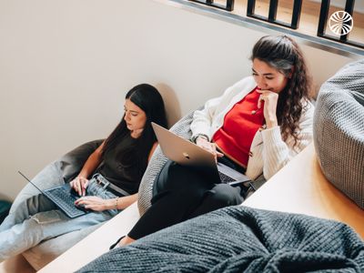 Two women working together on laptops in a cozy area.