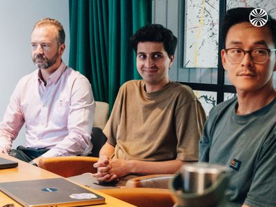 Three male colleagues of various ethnicities listening around a meeting table.