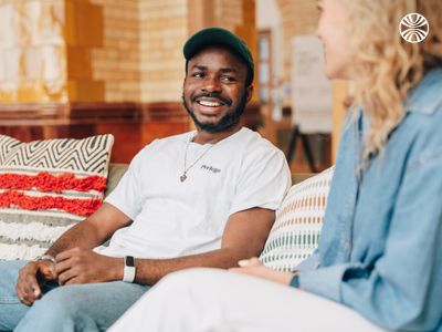 Black man smiling and chatting with a white colleague while sitting on a comfortable office couch.