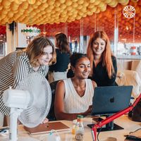 2 white women and one Black woman collaborating at a desk with a laptop in an office.