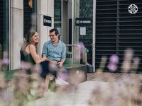 A man and a woman sit on a bench outside a building, smiling and chatting. Signs indicate a no-smoking area.