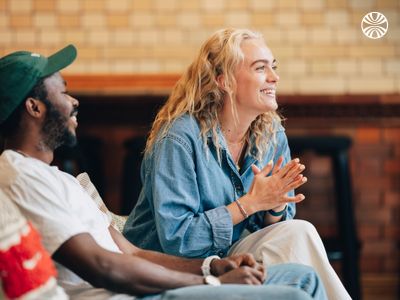 Black man and white woman sitting on a sofa, smiling and looking to their side.