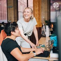 Two colleagues collaborate at a computer in a well-lit office.