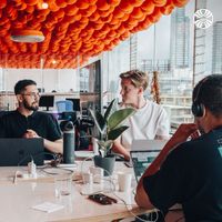 3 men collaborating at a table in an office with cityscape views.