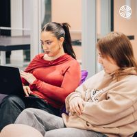 Two colleagues working together on a laptop in a casual seating area.