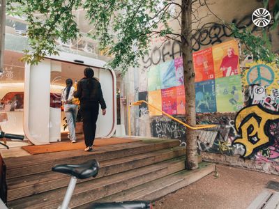 2 Black women entering a graffitied building with various posters on display.